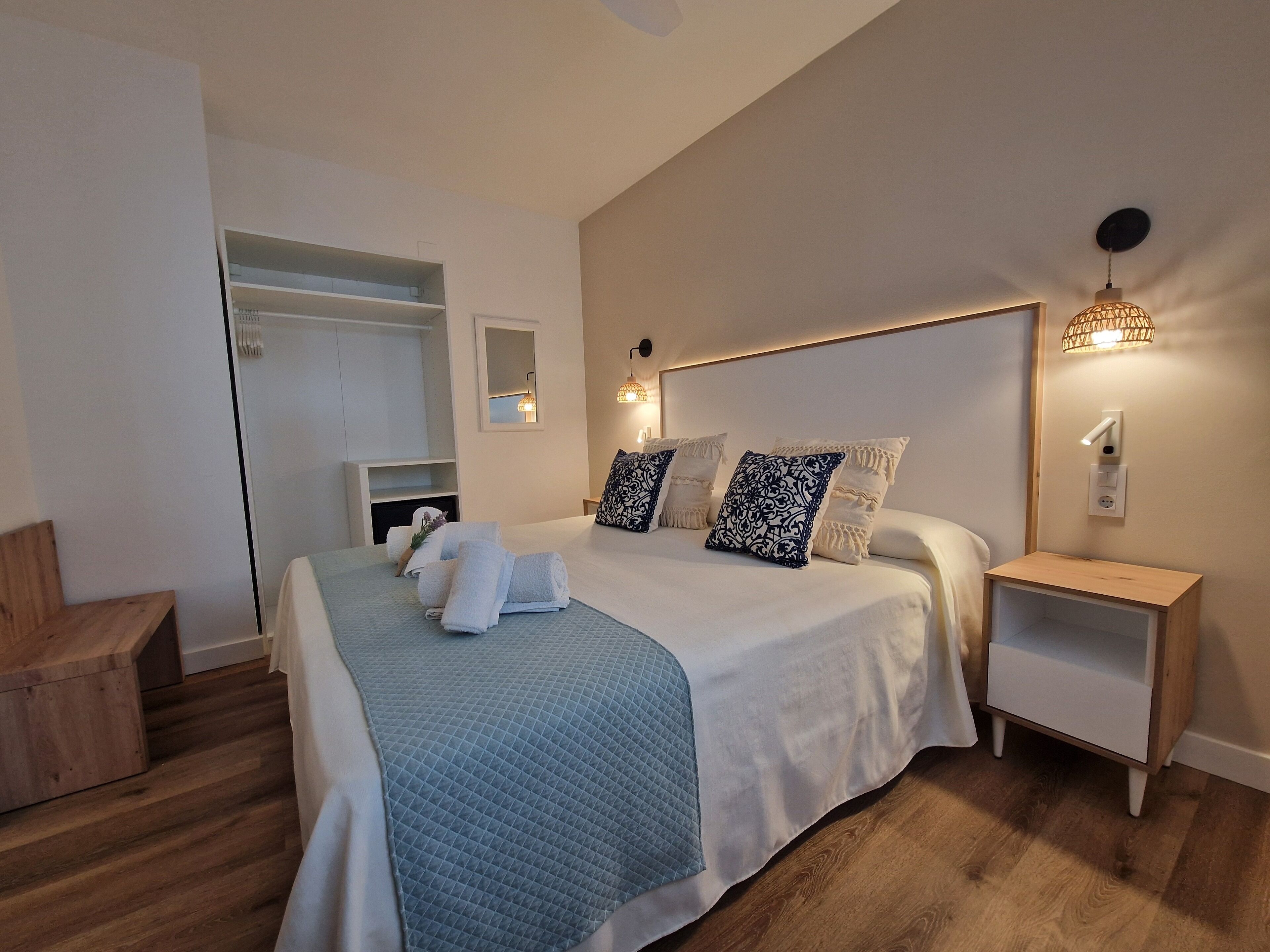 A modern bedroom with a large bed, bedside tables, a mirror, and a wardrobe.
