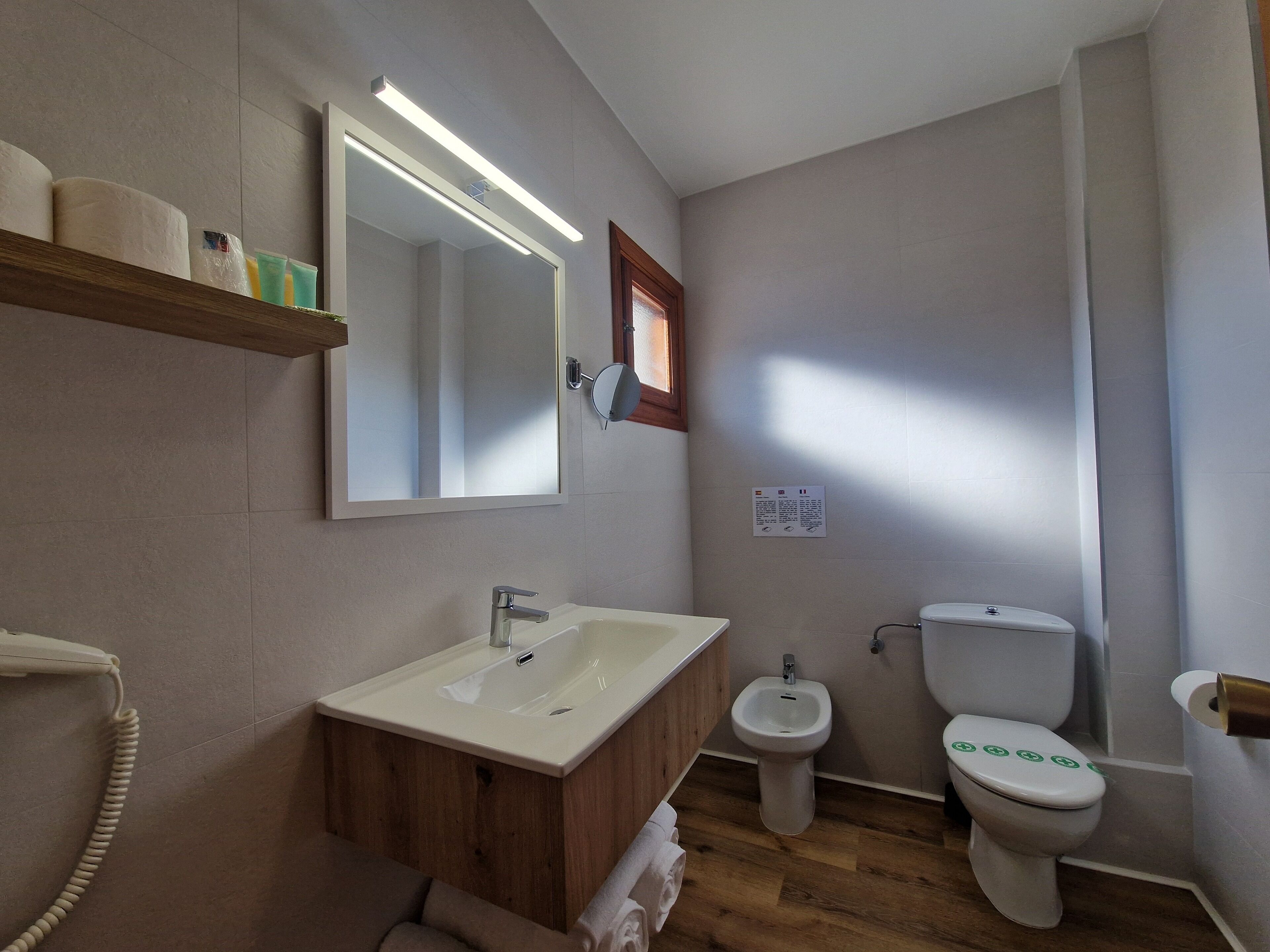 Un baño con tocador de madera, un lavamanos blanco, un bidé y un inodoro con iconos verdes.