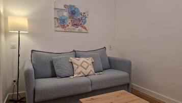 A grey sofa with a patterned cushion, a wooden coffee table, and a floor lamp.