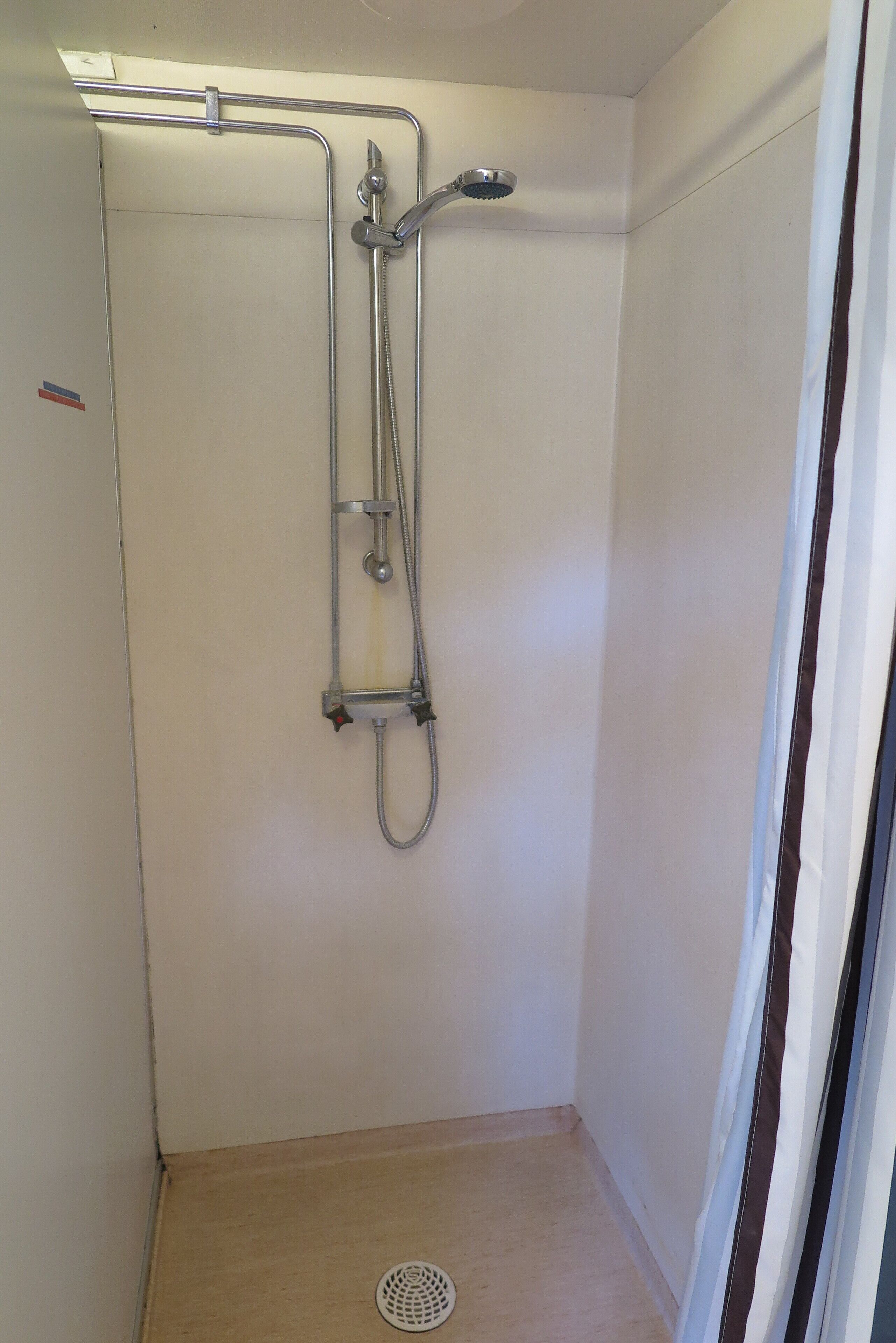 A small, enclosed shower area with a handheld showerhead and a fixed showerhead, a metal grab bar, and a drain.