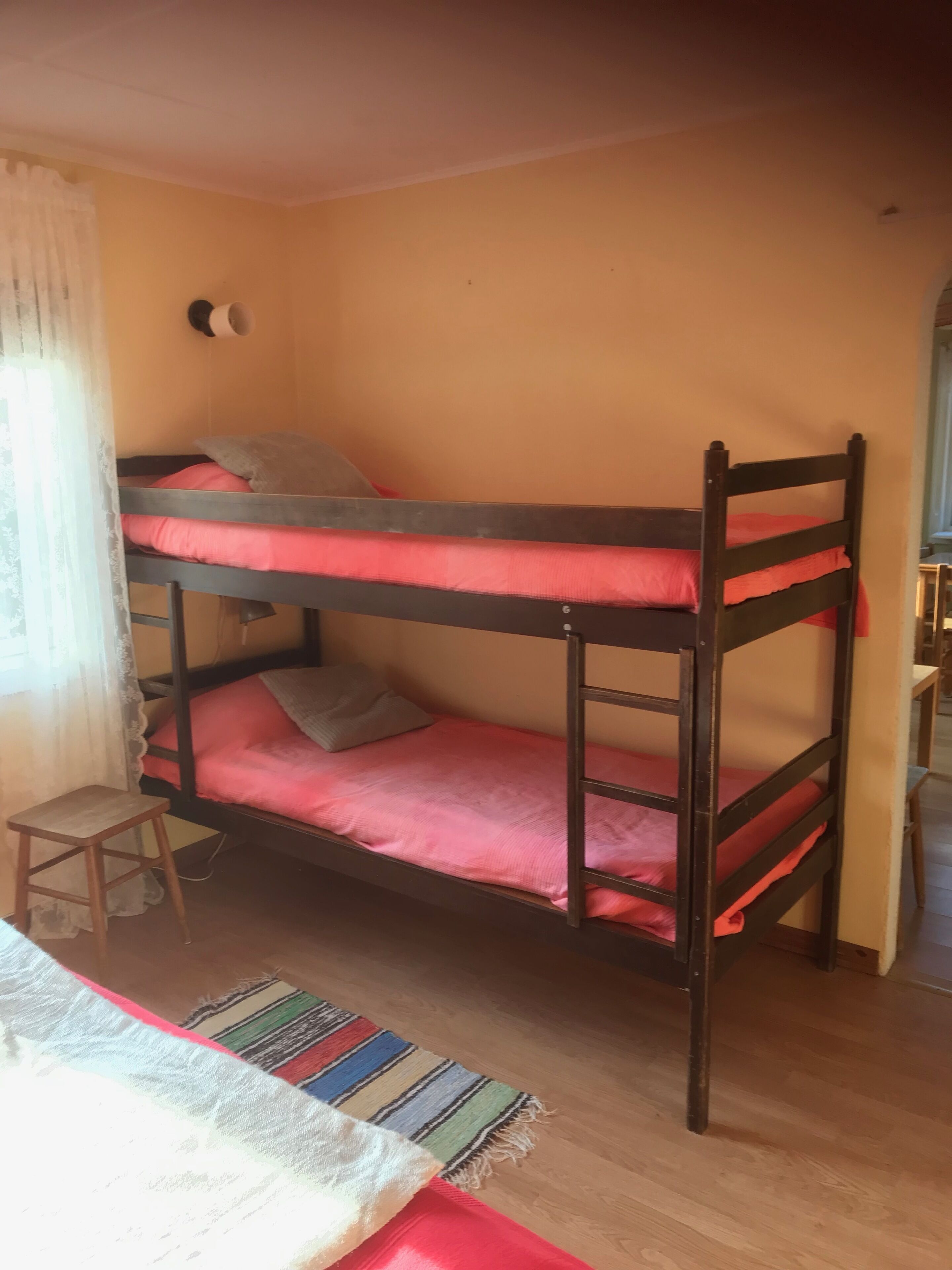 A bunk bed with two levels, a small wooden stool, and a colorful striped rug on a wooden floor.