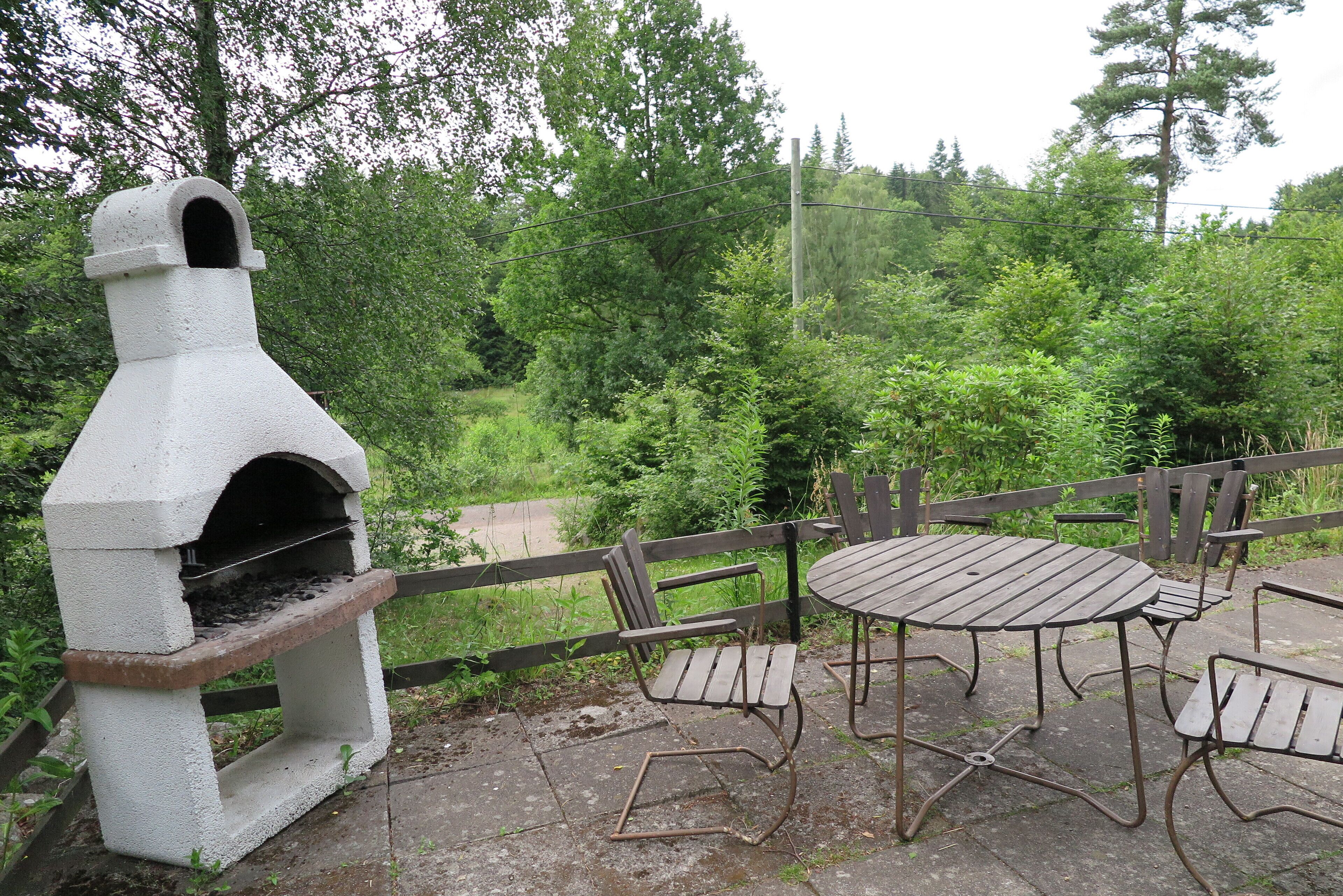 Eine Außenpatio mit einem Betonpizzaofen, Holzstühlen und einem Tisch.