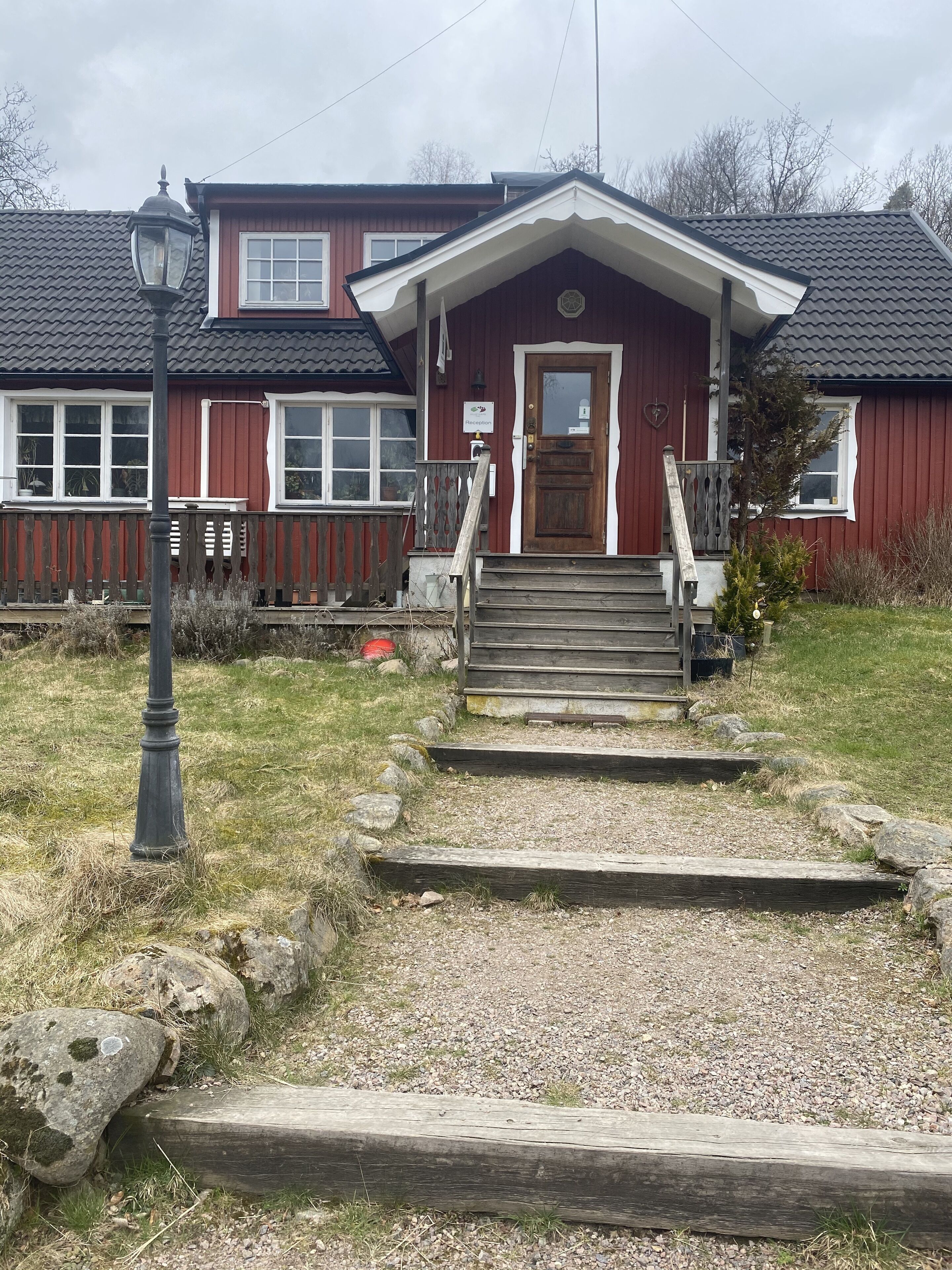 A two-story house with a red exterior, a front porch with steps, and a wooden fence.