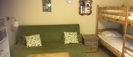 A room with a green sofa, a wooden table, a bunk bed, a clock, and a framed picture on the wall.