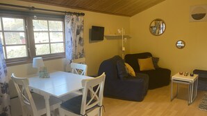 A cozy living area with a dining table, chairs, a sofa, and a small side table. - Ullstorps Stugor (Hoor)