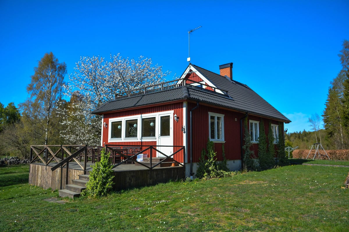 A red house with a sloped roof, a wooden deck, and a chimney.