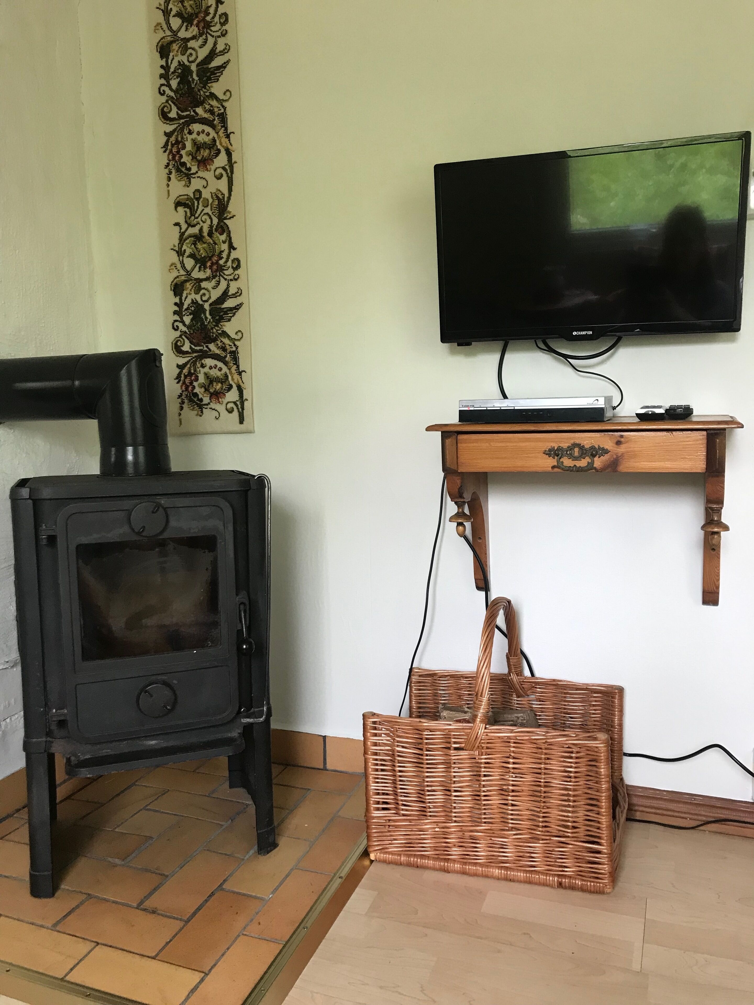 A room with a black wood-burning stove, a television mounted on the wall, and a wicker basket on the floor.