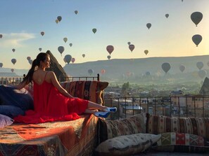 Una persona descansando en una cama con vistas a un paisaje urbano y globos aerostáticos en el cielo.