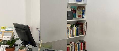 A reception desk with a computer, a clock, and a bookshelf with various books.