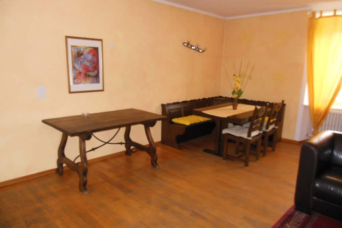 Un coin repas avec une table et des chaises en bois, un banc et un tableau accroché au mur.