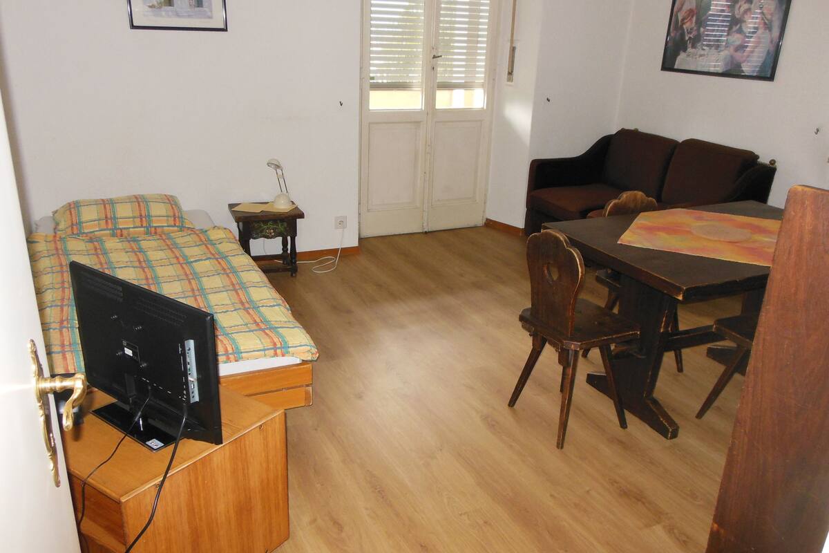 Une pièce de taille modeste comprenant un lit, un bureau avec un ordinateur, une table à manger avec des chaises et un canapé.