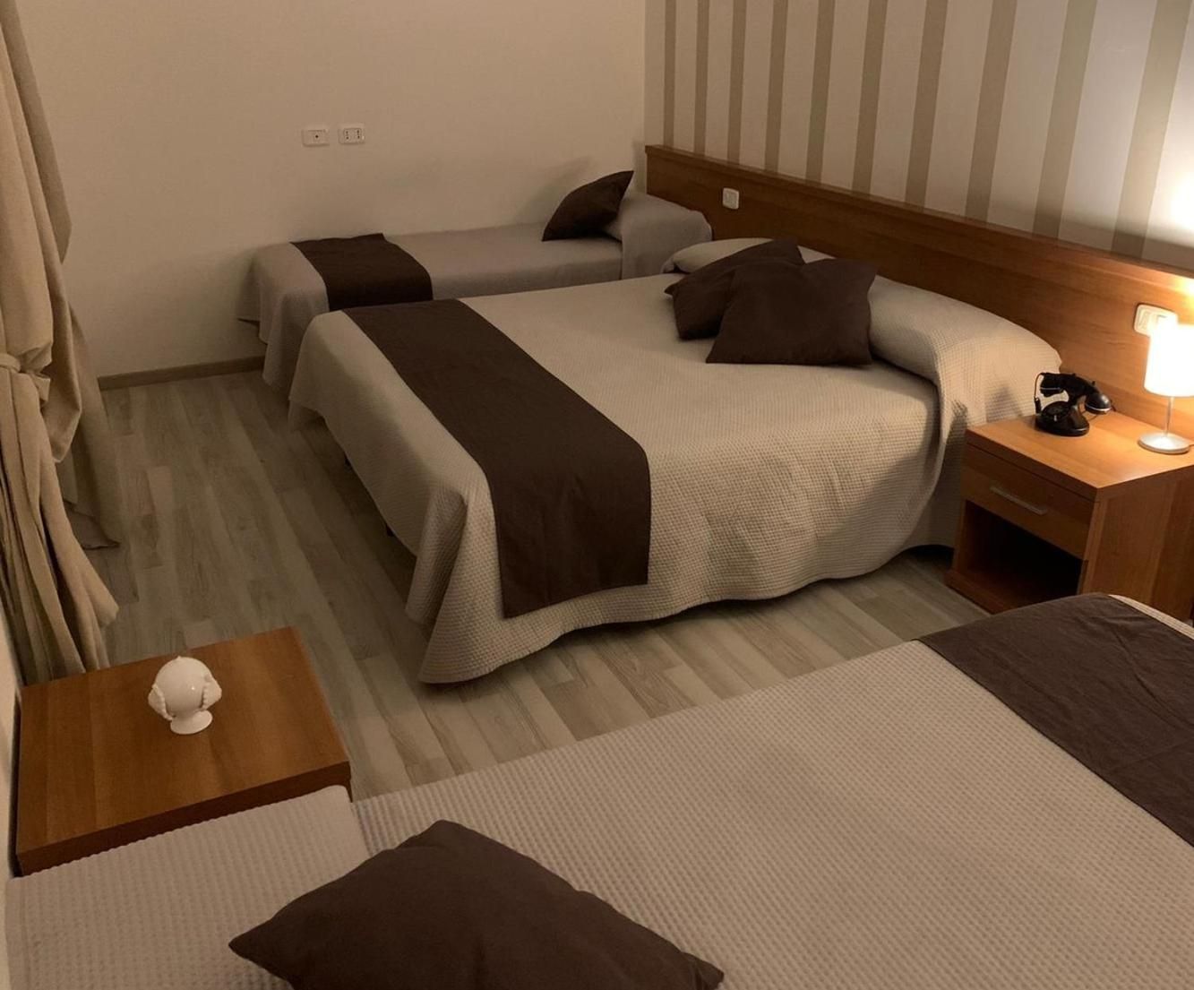 A hotel room with two beds, a bedside table with a lamp, and a small table with a decorative item.