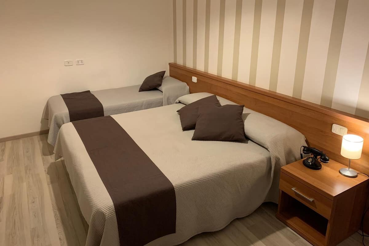 A hotel room with two beds, a nightstand with a lamp, and a striped wall.