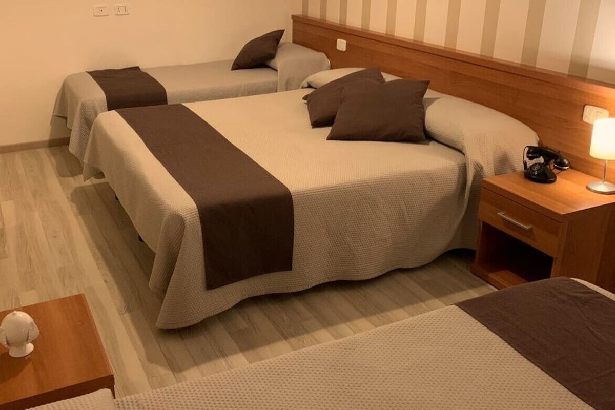 A hotel room with two beds, a nightstand with a lamp, and a small table with a decorative item.