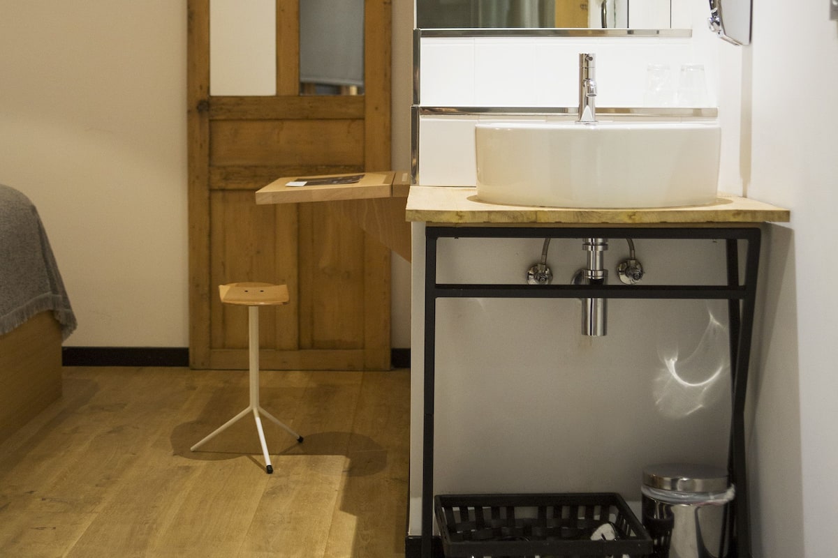 A bathroom with a wooden door, a white sink, a mirror, and a small stool.
