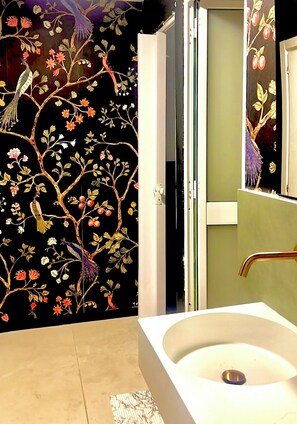 Un baño con lavamanos blanco, un espejo y una puerta con papel tapiz floral.