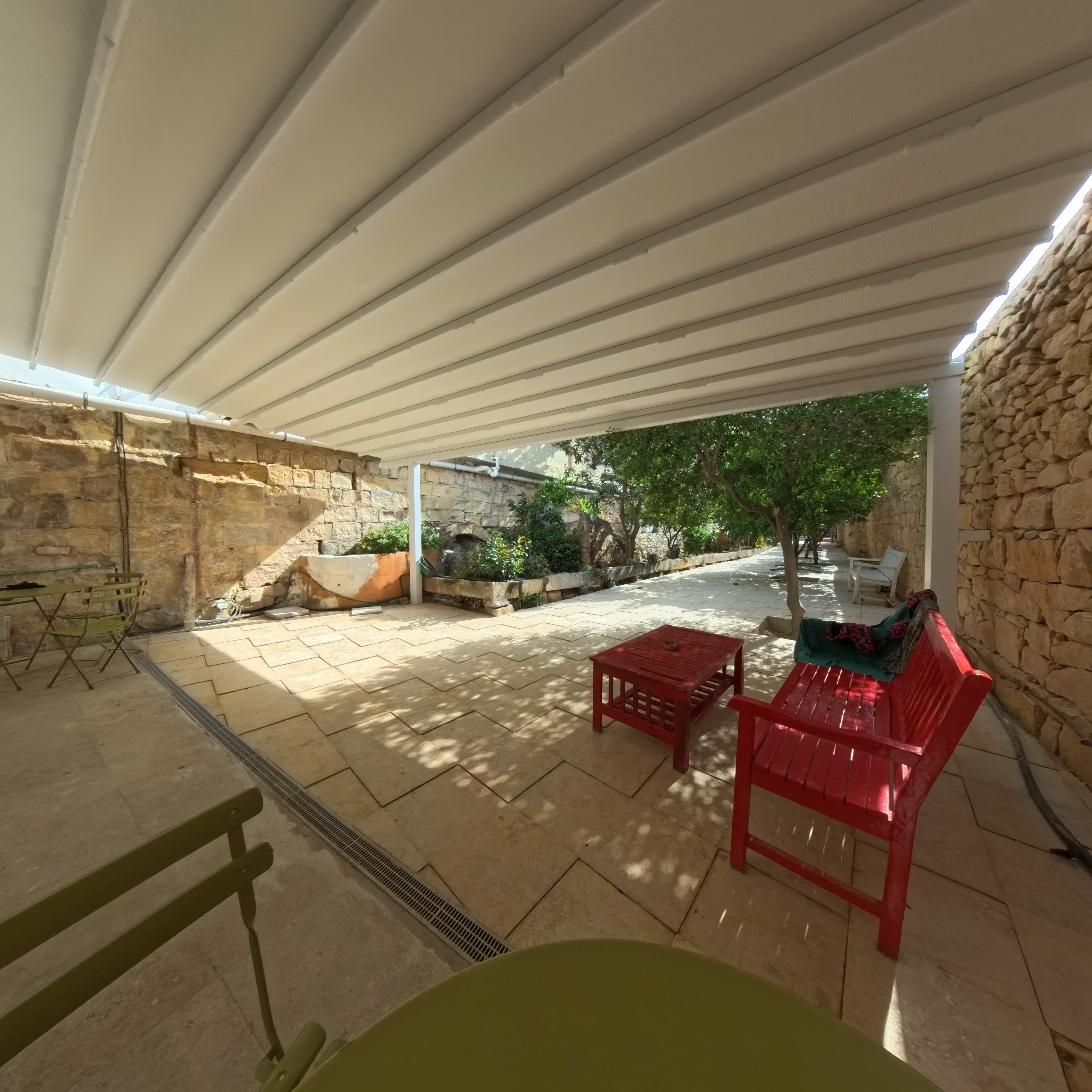 An outdoor patio with stone walls, a covered seating area, and a view of the garden.