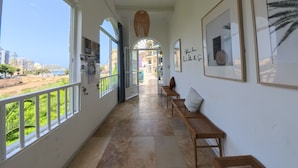 Un pasillo con vista al mar, bancos de madera y obras de arte enmarcadas en las paredes.
