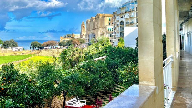 Un balcón con vista a un paisaje urbano costero, que incluye edificios históricos y un cielo despejado.