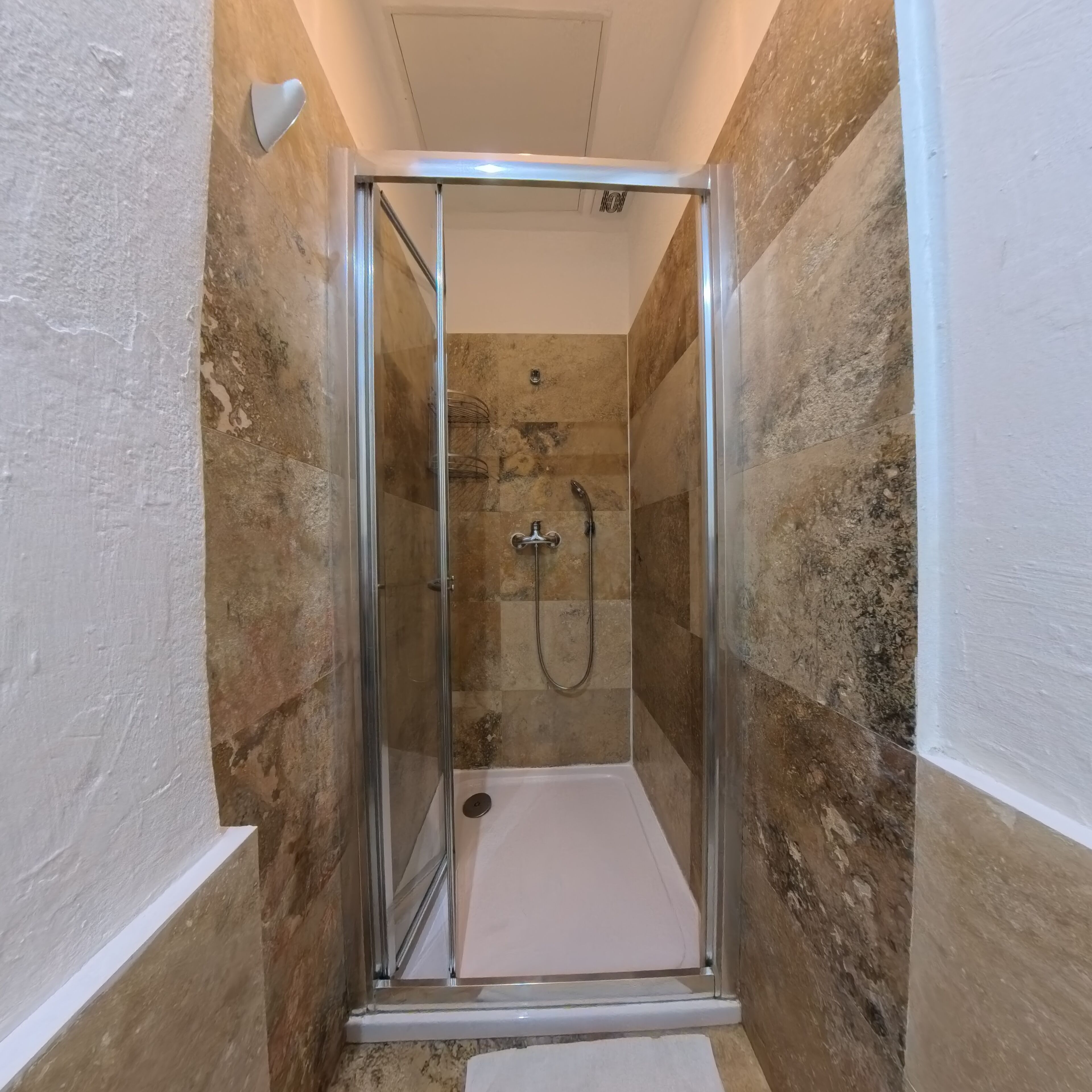 A small, enclosed shower area with a glass door, tiled walls, and a white floor.