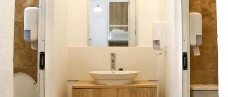 A small, modern bathroom with a wooden vanity, a sink, a mirror, and two toilets.