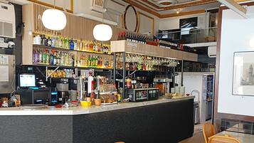 Zona de bar con mostrador, estantes llenos de botellas y un letrero de cerveza Amstel. Hay sillas de mimbre y una mesa preparada para comer.