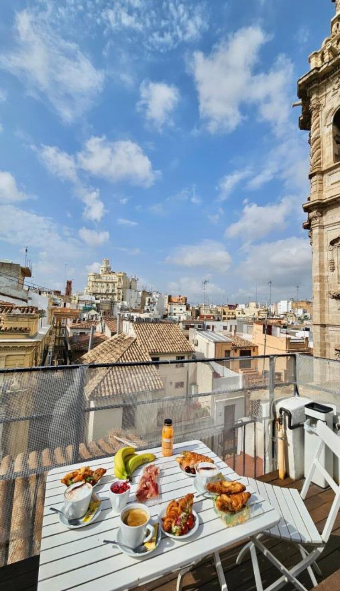 Mesa dispuesta con comida y bebidas en una terraza en la azotea con vista a la ciudad.