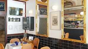 Interior de restaurante con techos altos, detalles dorados ornamentales y una zona de bar visible a través de un espejo grande.