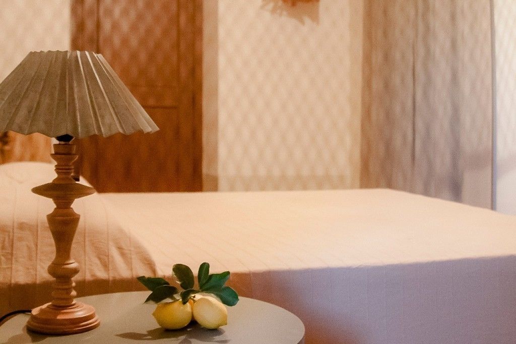 A bed with a white cover, a wooden lamp on a bedside table, and a small plant with green leaves and yellow flowers.