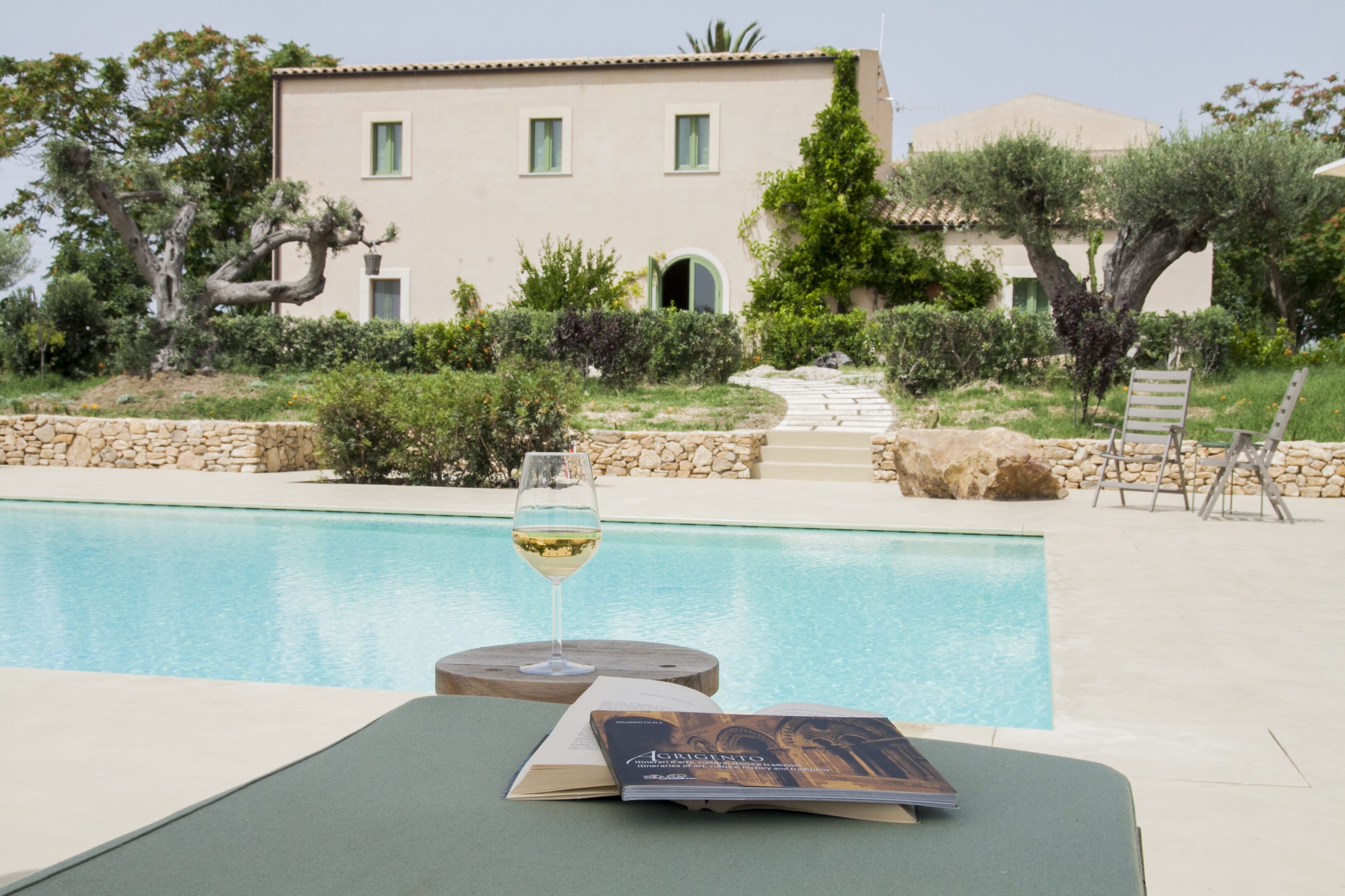 A poolside area with a book and a glass of wine on a lounge chair.