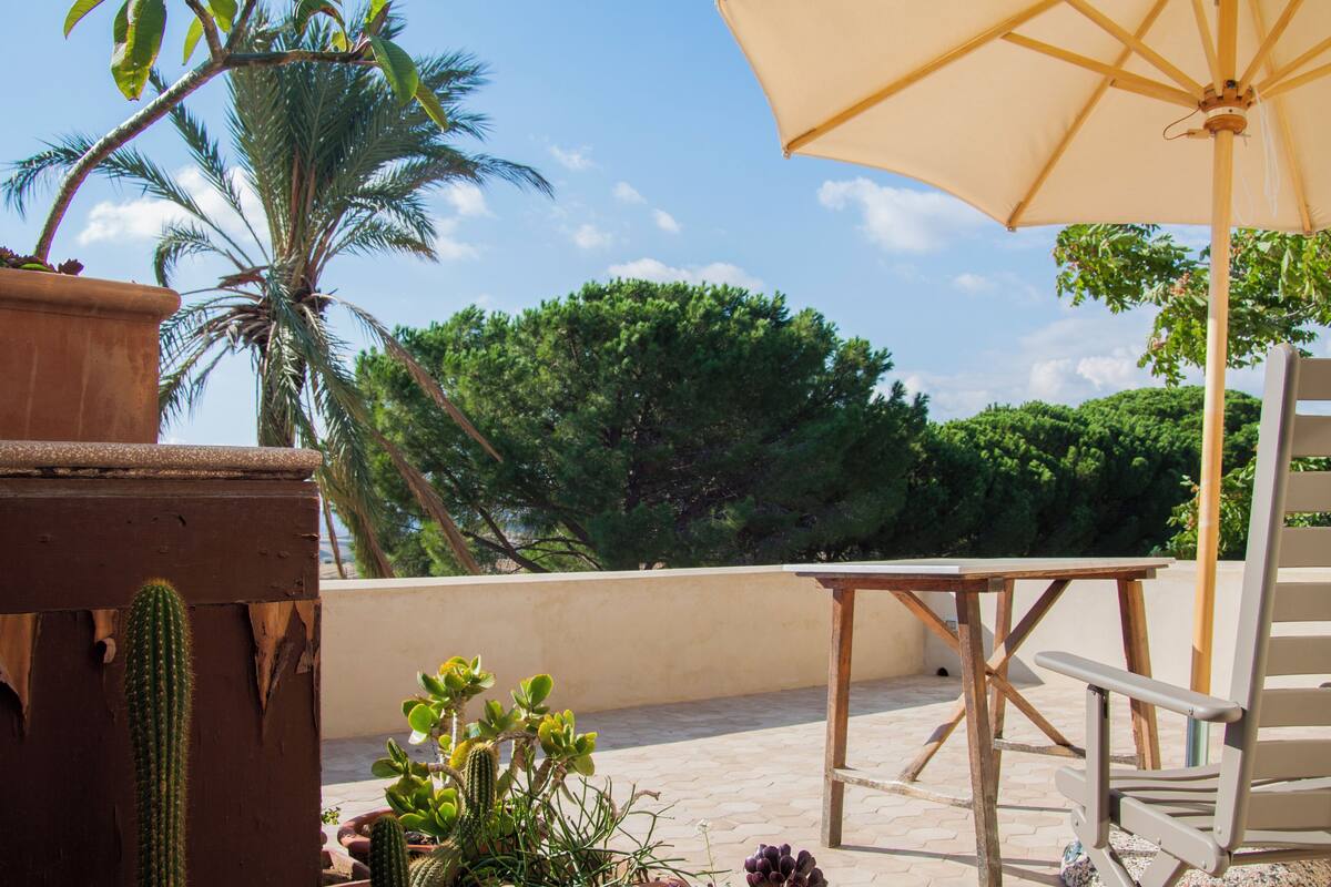 Un patio con una mesa de madera, una sombrilla color beige y una silla.