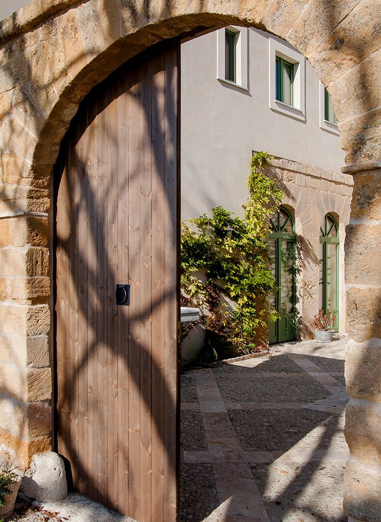 Un arc en pierre mène à un bâtiment doté d’une porte en bois et de volets verts.