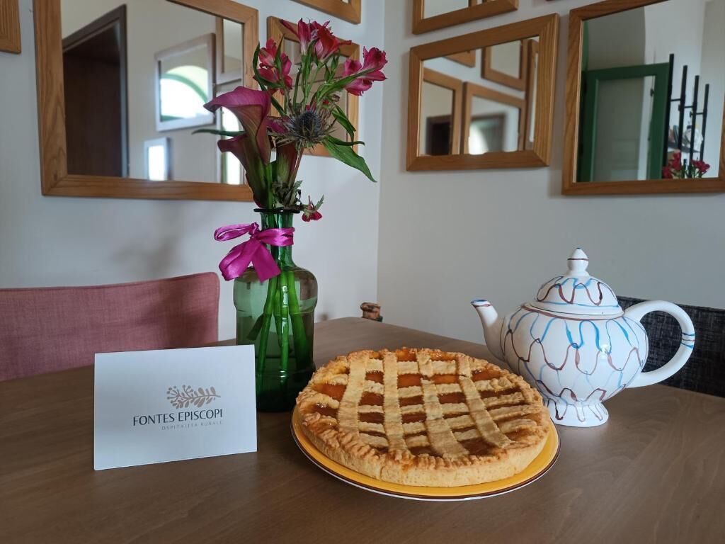 A table with a pie, a vase with flowers, a teapot, and a sign.