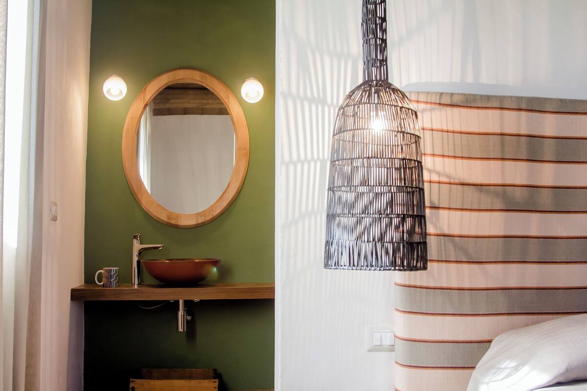 Un baño con lavamanos de madera, un espejo, una lámpara colgante y cortinas a rayas.