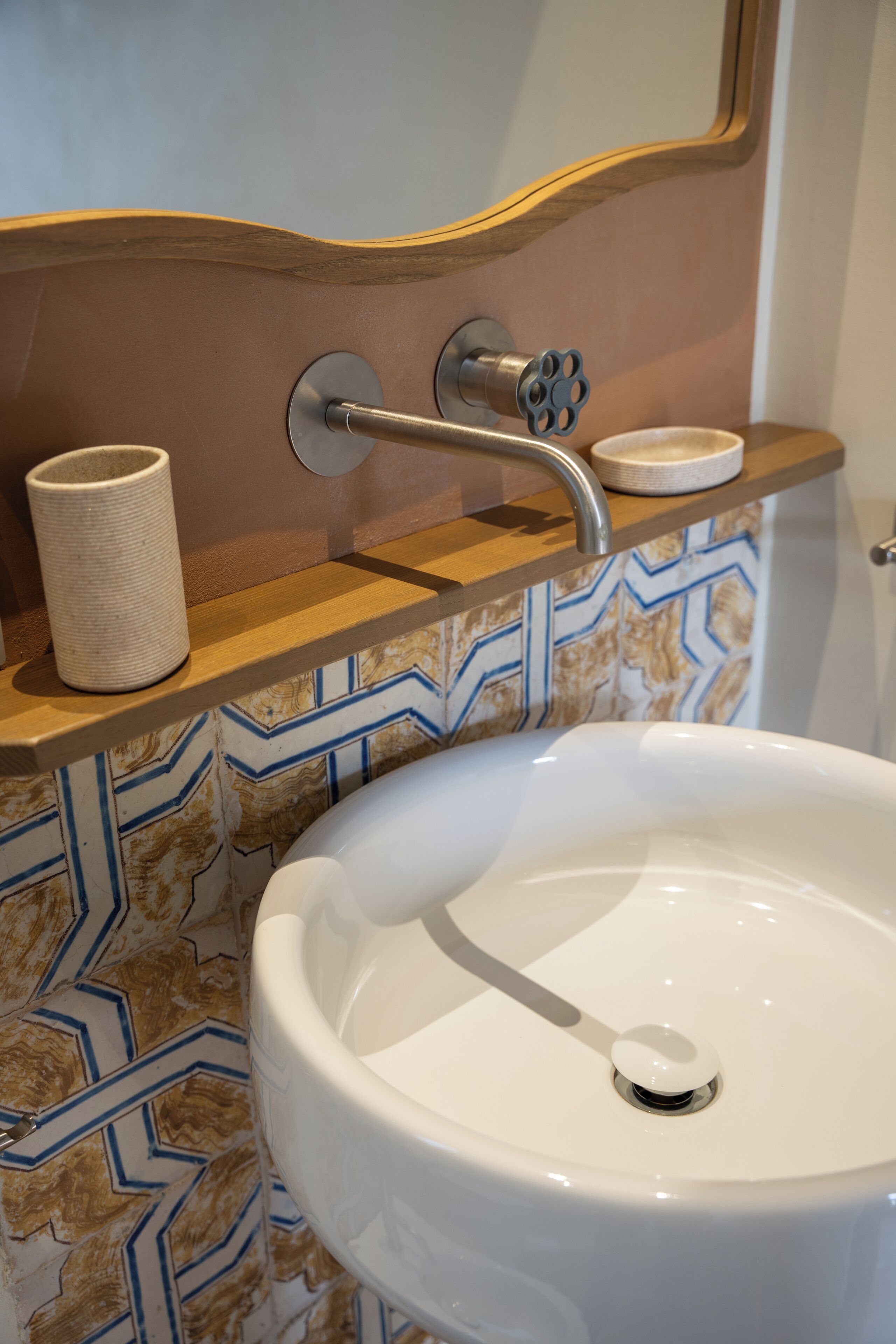 Une salle de bain avec un lavabo blanc, un distributeur de serviettes et un porte-gobelet sur une étagère en bois.
