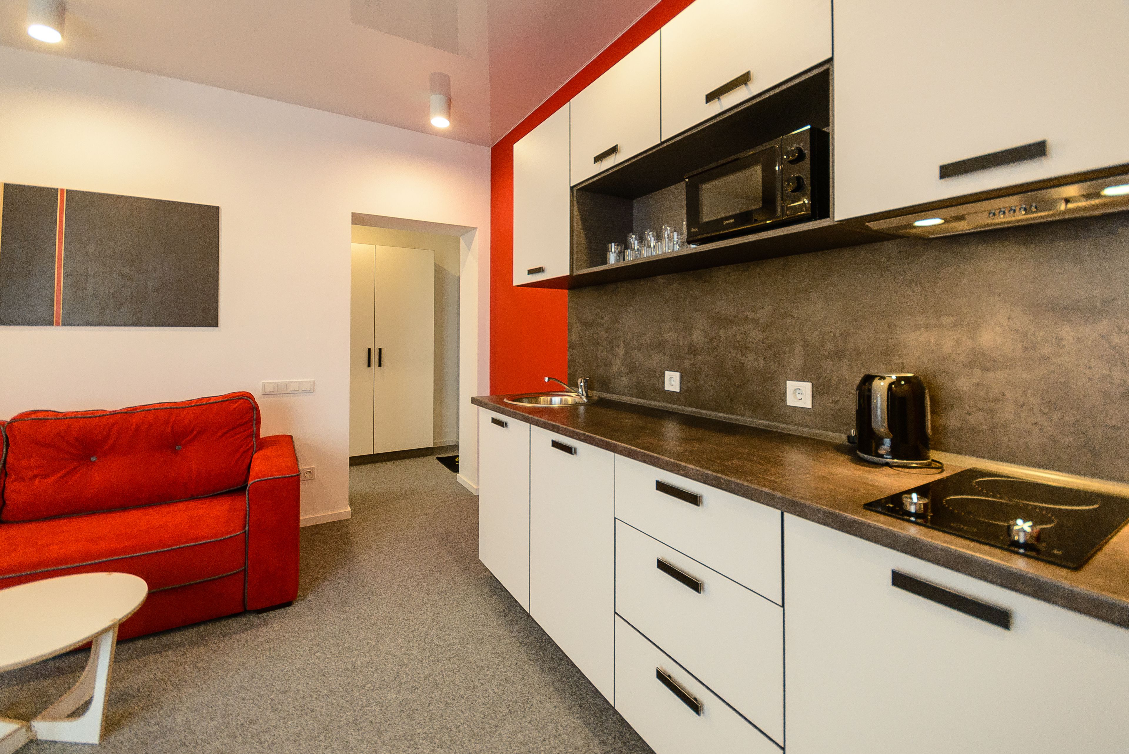 A modern kitchen with white cabinets, a red sofa, and a coffee machine.