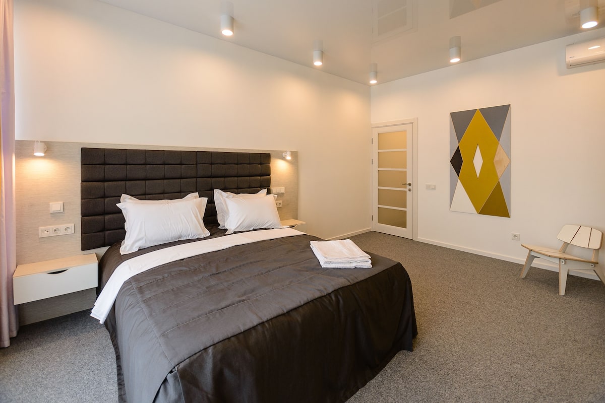 Una habitación de hotel moderna con una cama grande, una mesita de noche, una silla y una obra de arte colgada en la pared.