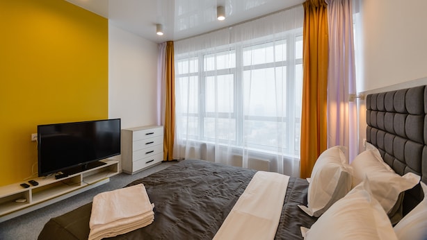 Habitación de hotel con cama, televisión, cómoda y ventana con cortinas.