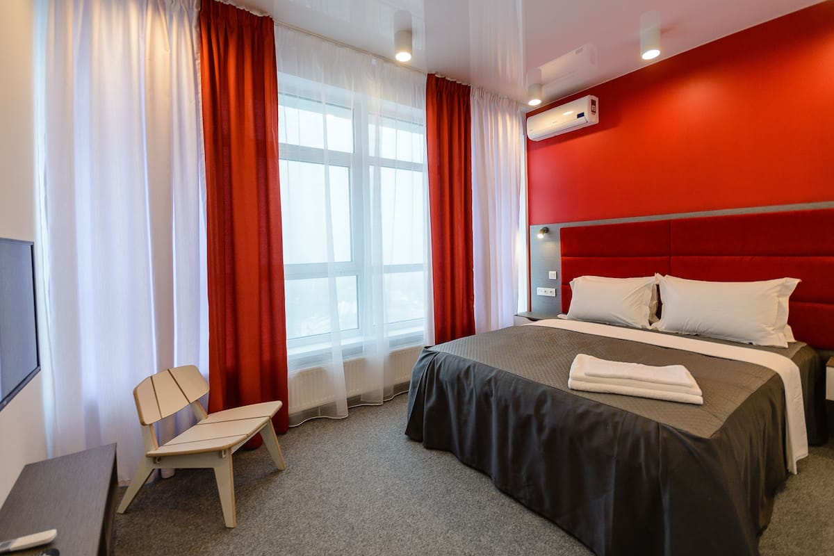 Una habitación de hotel con cama, una silla, un escritorio y una ventana con cortinas.