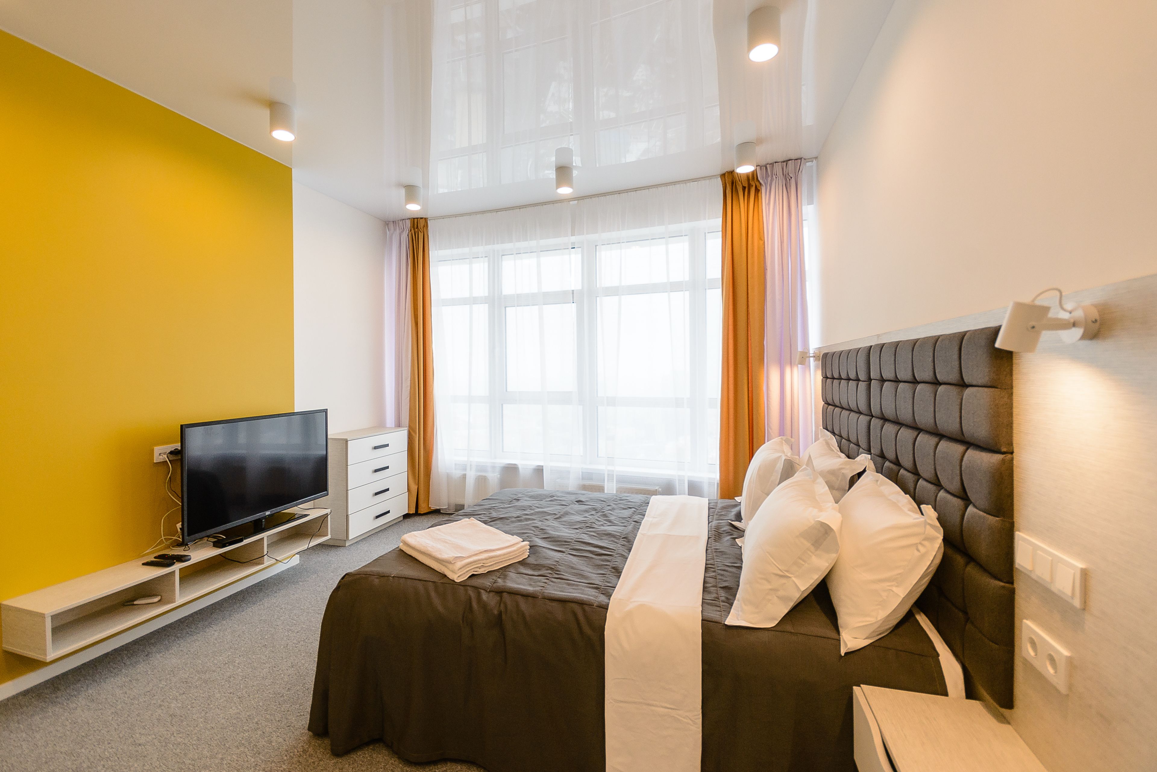 A modern hotel room with a large bed, a flat-screen TV, a bedside table, and a window with curtains.