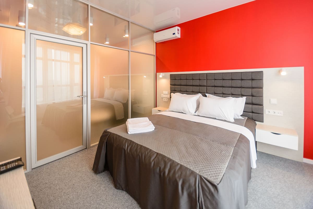 Habitación de hotel con una cama grande, armario con puerta corredera de vidrio y una pared de acento roja.