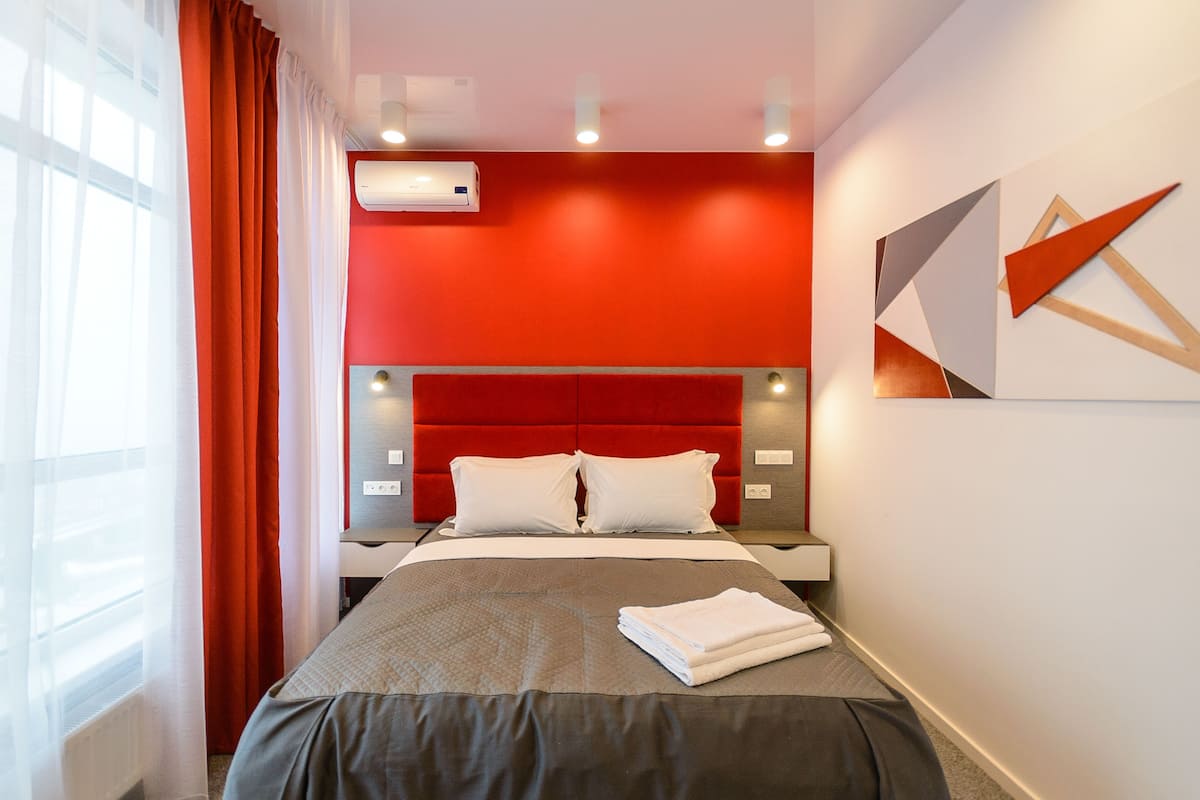 Habitación de hotel con una pared de acento rojo, una cama moderna con almohadas blancas y una toalla doblada con cuidado sobre la cama.