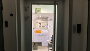Entrada de hotel con mostrador de recepción, cartel de casa de huéspedes y panel informativo del tiempo.