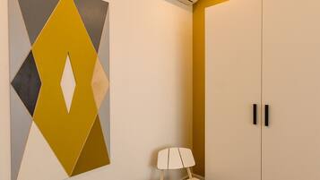 A room with a geometric wall art, a white wardrobe, a small wooden chair, and an air conditioning unit.
