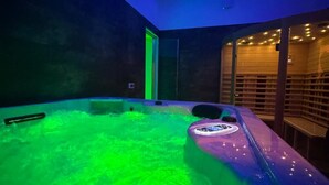 Un spa moderno con una tina de hidromasaje grande, climatizada e iluminada en verde, y un banco de madera.