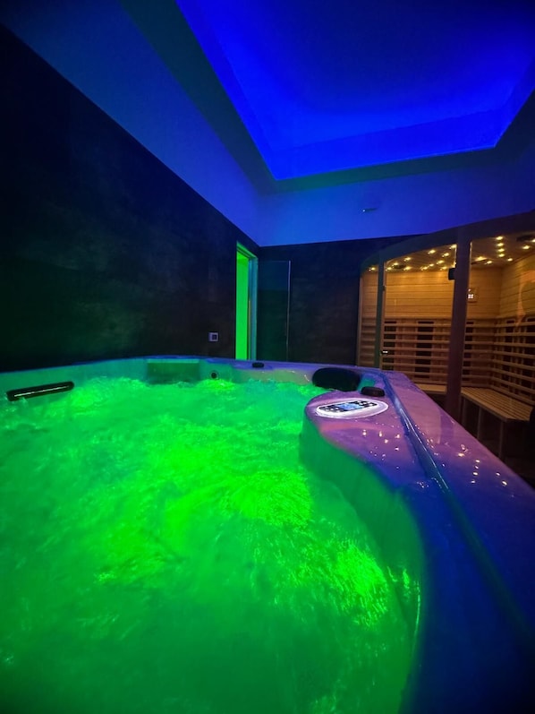 A modern spa room with a large, heated, green-lit hot tub and a wooden bench. - Hotel Butterfly & YoUnique Spa (Rimini)