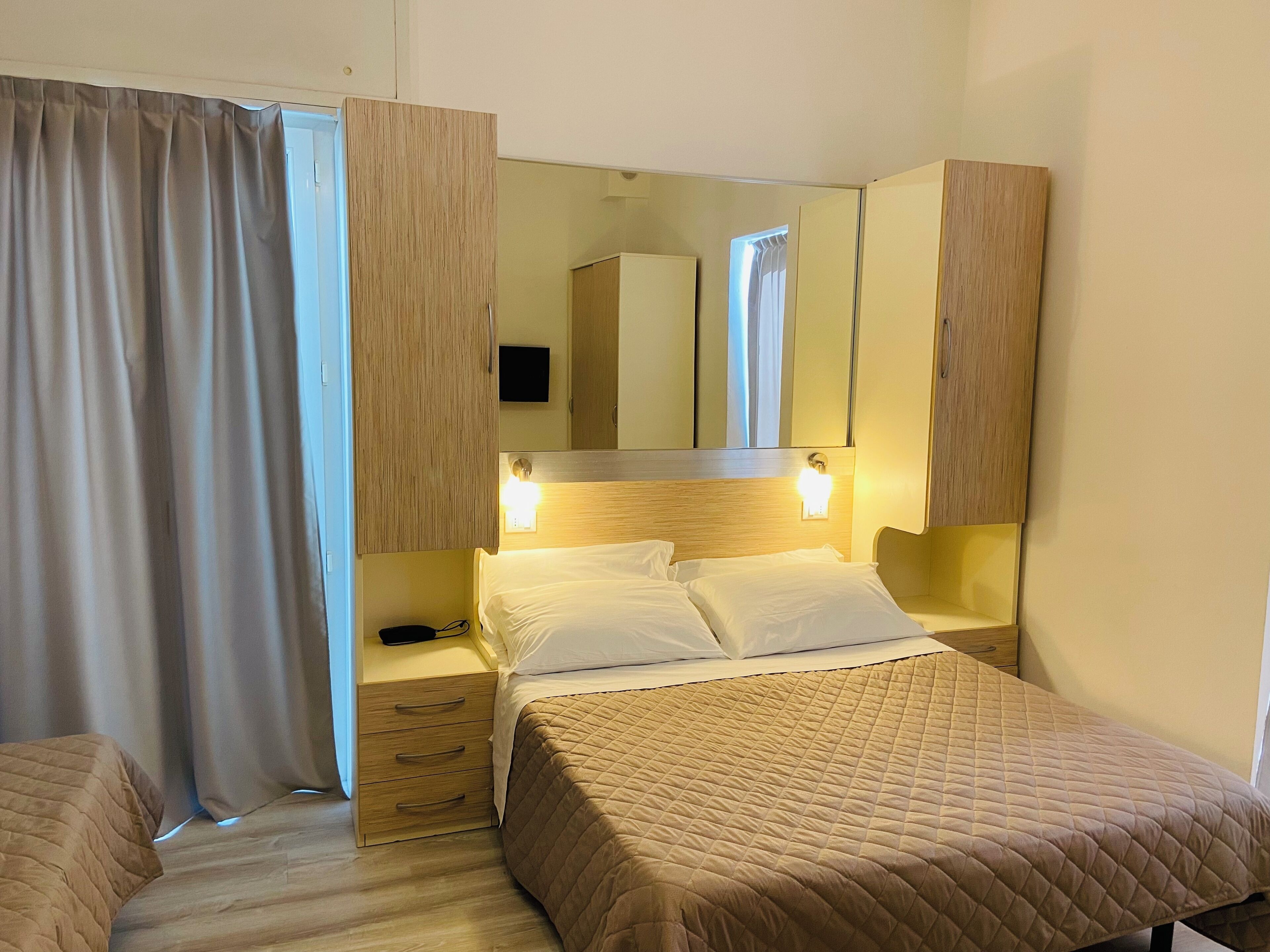 Una habitación de hotel con cama, mesitas de noche, armario y espejo.