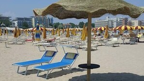 Una playa con tumbonas y sombrillas, una estructura de sombrilla de paja y edificios al fondo.
