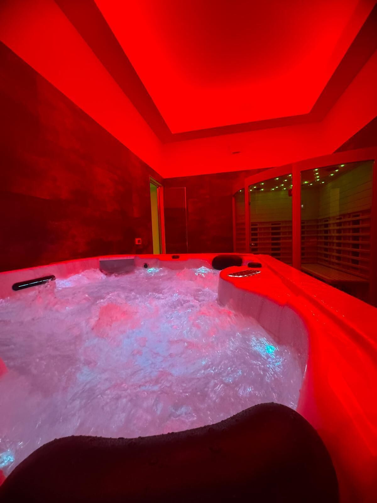 Un bain à remous dont l’intérieur est éclairé de lumières rouges, et qui est entouré d’une paroi en verre.