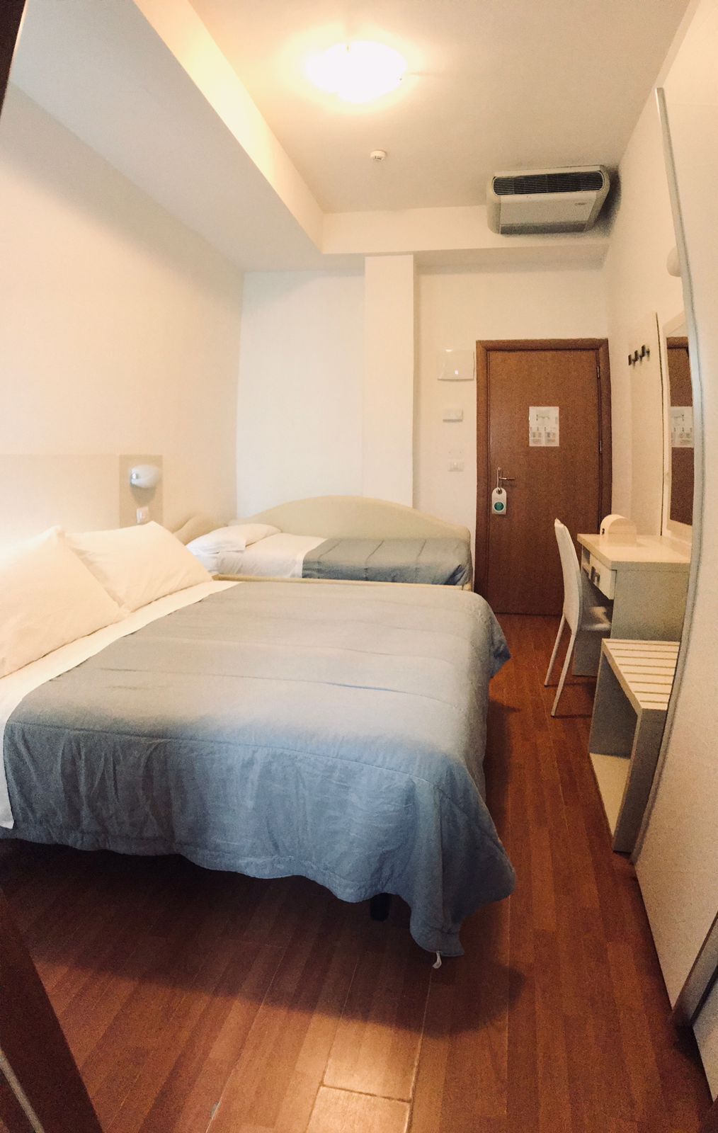 A hotel room with two beds, a desk, a chair, a mirror, and a door.